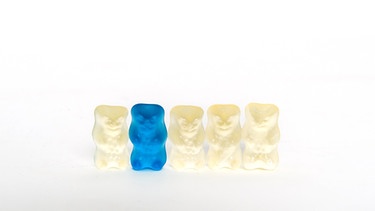 Ein blaues Gummibärchen steht in einer Reihe von weißen Gummibärchen. | Bild: Natasha Heuse