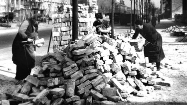 Drei Frauen in zerstörter Stadt, die Ziegelsteine sortieren | Bild: picture-alliance/dpa