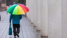 Eine Person läuft unter einem Schirm durch den Regen. | Bild: BR/Leon Baatz