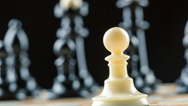 Eine weiße Schachfigur steht vor einer Reihe von schwarzen Schachfiguren. | Bild: colourbox.com