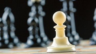 Eine weiße Schachfigur steht vor einer Gruppe von schwarzen Schachfiguren. | Bild: colourbox.com