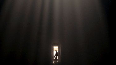 Die Silhouette eines Menschen in der Ferne, die von einem Licht von oben beleuchtet wird | Bild: picture-alliance/dpa