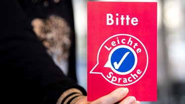 Eine Frau hält Informationsmaterial zum Thema "Leichte Sprache" mit der Aufschrift "Bitte Leichte Sprache" in den Händen.
| Bild: picture alliance / dpa / Sven Hoppe