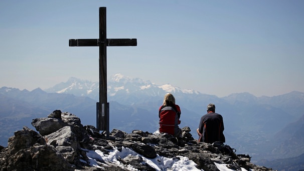 Zwei Wanderer sitzen auf dem Gipfel neben dem Gipfelkreuz | Bild: picture-alliance/dpa