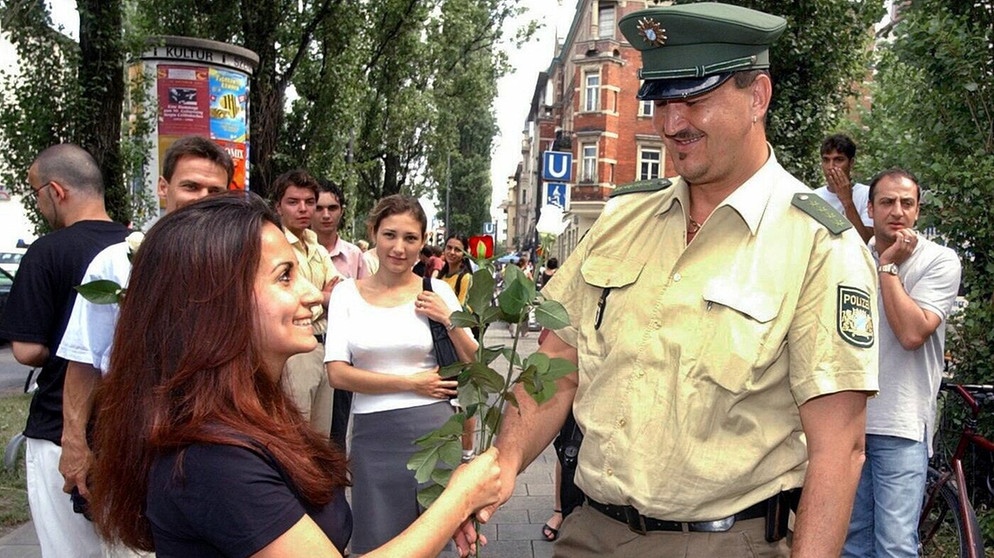 Eine junge Türkin schenkt einem Polizeibeamten am 21.6.2002 an der Münchner Leopoldstraße eine Rose. Mit 5000 weiß-roten Rosen haben sich die türkischen Fußballfans bei ihren Münchner Mitbürgern bedankt.  | Bild: picture-alliance/dpa