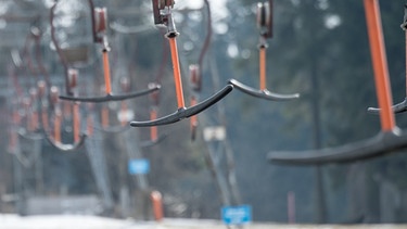 Die Bügel eines Schlepplifts hängen am 28.02.2016 in Sankt Englmar (Bayern) im Bayerischen Wald neben einer Skipiste mit wenig Schnee. | Bild: picture-alliance/dpa/Armin Weigel