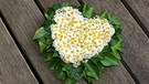 Ein Herz aus Efeu und Gänseblümchen liegt während einer Hochzeit auf einem Steg. | Bild: picture-alliance/dpa