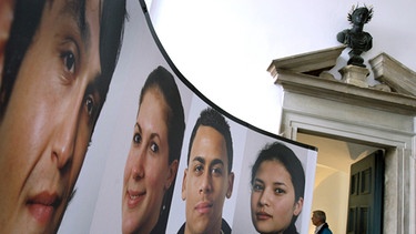 Überdimensionale Porträts jugendlicher Migranten, die in Augsburg leben, sind 2008 in einer Ausstellung im Foyer des Rathauses von Augsburg unter der Büste von Kaiser Augstus zu sehen.  | Bild: picture-alliance/dpa