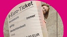 Ann-Kathrin Mittelstraß, Host des Zündfunk-Podcasts „Die Sache ist die …“, lugt hinter einem überlebensgroßen 9-Euro-Ticket hervor | Bild: BR/ Paula Lochte