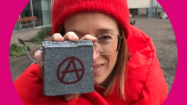 Die Sache ist die-Host Ann-Kathrin Mittelstraß mit einem Pfllasterstein, auf den ein Anarchy-Zeichen gemalt ist | Bild: Tom Kretschmar/BR
