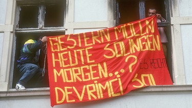 Auf dem Bild sieht man zwei Menschen, die aus einem Hausfenster ein rotes Banner halten. Darauf steht: Gestern Müllen, heute Solingen, morgen...?
| Bild: picture alliance / Caro | Trappe