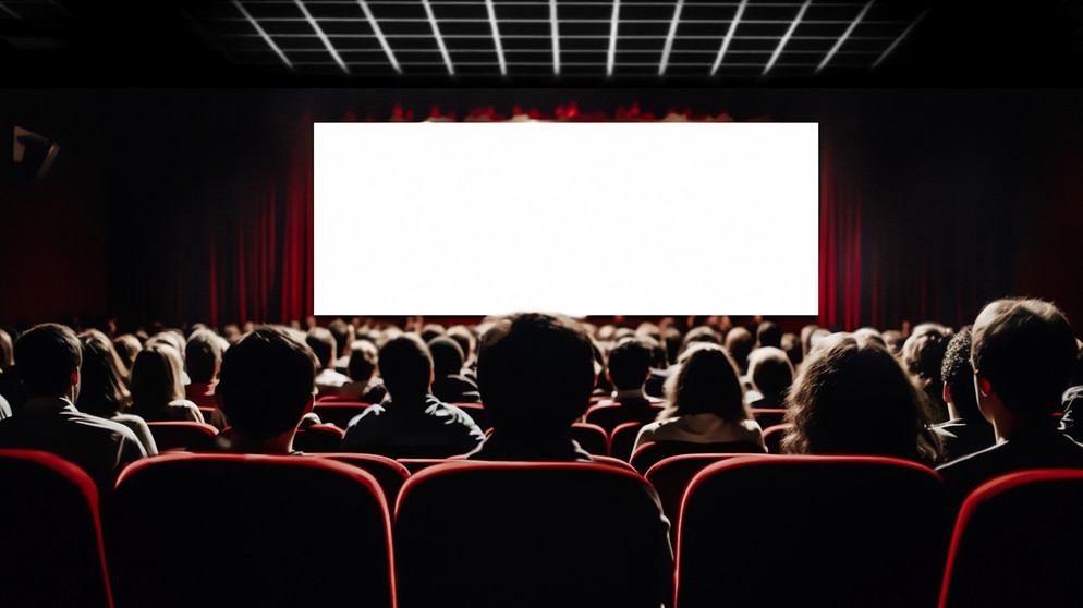 Menschen sitzen in einem voll besetzten Kinosaal und schauen auf eine weiße Kinoleinwand. | Bild: stock.adobe.com/Soho A studio