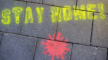 Ein Graffiti mit "Stay Home" und einem Virus auf einer Münchner Straße | Bild: picture-alliance/dpa