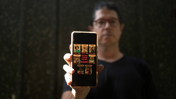 Yuval Haran, whose family is celebrating the return of his mother, his sister, and four others from Hamas captivity in the Gaza Strip, poses for a portrait with a picture on his phone of his family's hostage posters. | Bild: picture alliance / ASSOCIATED PRESS | Maya Alleruzzo