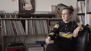 DJ und Komponistin Lena Willikens erzählt vor Plattenregalen sitzend im Dokumentarfilm "The Sound Of Cologne" von ihren Erfahrungen | Bild: TelevisorTroika