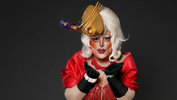 Fernsehmoderator Sükrü Pehlivan tritt als Dragqueen Boobie Gold in der Fernsehsendung "Viva la Diva" auf. Er trägt ein rotes Kleid zu weißen Haaren und einem Hut aus Lampen. | Bild: RTL / Frank W. Hempel