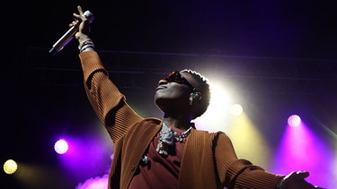 Rapper Wizkid aus Nigeria steht auf einer Bühne und zeigt mit dem Mikrofon in den Himmel | Bild: picture-alliance/dpa