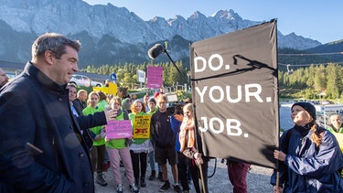 Markus Söder (l, CSU), Ministerpräsident von Bayern, unterhält sich vor Beginn seiner Klimatour in der Zugspitzregion (hinter dem Banner "Do. Your. Job.") mit jugendlichen Greenpeace und Bund Naturschutz Aktivisten.  | Bild: dpa-Bildfunk / Peter Kneffel