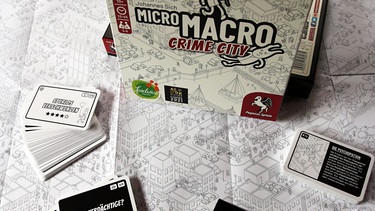 19.07.2021, Berlin: "MicroMacro: Crime City" ist zum Spiel des Jahres 2021 gewählt worden. Ein großes Schwarzweiß-Poster und ein paar Karten ist alles was die Spieler brauchen um anhand des Stadtplans im Wimmelbildstil Dutzende Mord-und Todesfälle aufzuklären. | Bild: Wolfgang Kumm/dpa +++ dpa-Bildfunk +++