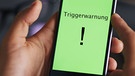 Symbolbild: Hinweis "Triggerwarnung" auf dem Bildschirm eines Smartphones | Bild: colourbox.com; Montage: BR