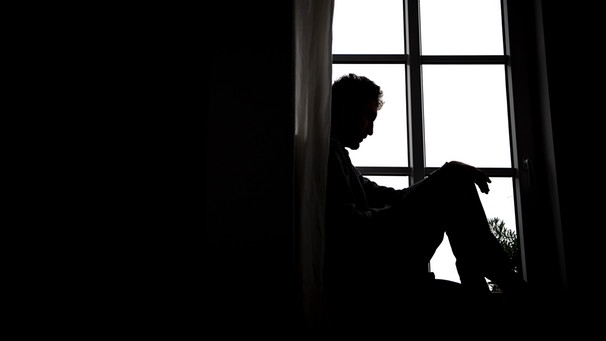 Ein Mann sitzt in Kauerhaltung vor einem Fenster. Man sieht nur Schatten und Konturen. Offensichtlich ist der Mann geknickt oder depressiv. | Bild: dpa-Bildfunk/Sina Schuldt