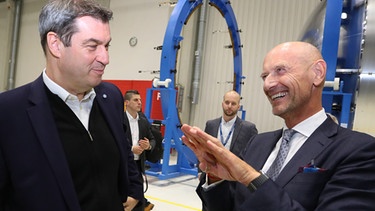 Markus Söder (CSU,l), bayerischer Ministerpräsident steht mit Hans Steininger, Vorstand von MT Aerospace in einer Fertigungshalle des Raumfahrtunternehmens MT Aerospace vor einem Teil der Ariane 6 Rakete. | Bild: picture-alliance/dpa