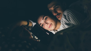 Paar schuat im Bett auf ein Handy | Bild: mauritius-images
