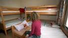 Frau sitzt mit dem Rücken zur Kamera auf einem Bett, vor sich Stockbetten für Kinder | Bild: picture-alliance/dpa