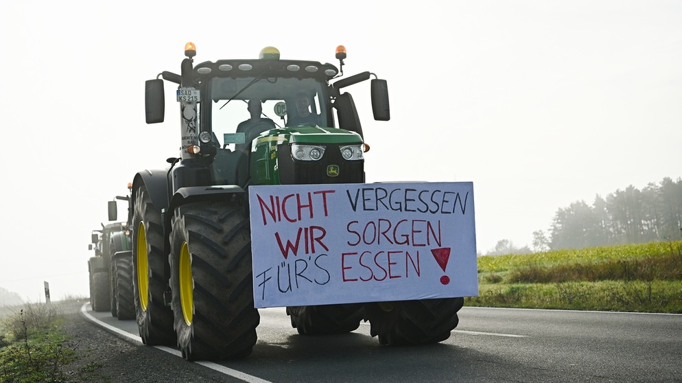 "Nicht vergessen wir sorgen für´s Essen", steht auf einem Transparent, das auf die Front eines Traktors montiert ist.  | Bild: Nicolas Armer / picture alliance / dpa
