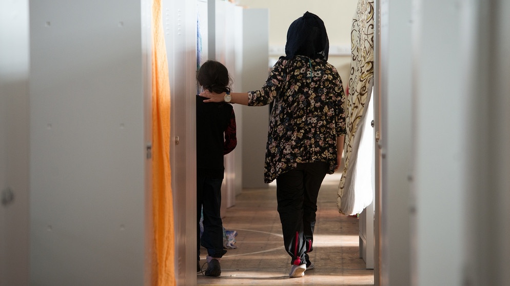 Frau mit Kind zwischen Metallschränken in einer bayerischen Flüchtlingsunterkunft | Bild: picture-alliance/dpa/Armin Weigel
