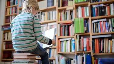 Ein Kind sitzt auf einem Bücherstapel und liest ein Buch | Bild: picture alliance / ZB | Thomas Eisenhuth