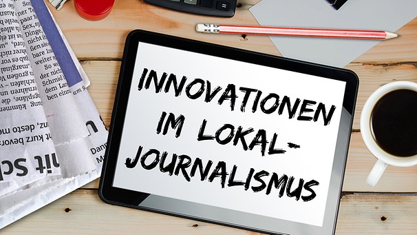 Ein Schreibtisch mit Zeitungen, Kaffeetasse, Stift und einem Tablet auf dem "Innovationen im Lokaljournalismus" geschrieben steht | Bild: colourbox.com; Montage: BR
