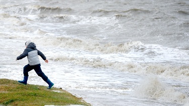 Ein Junge rennt am Strand von Harlesiel vor den peitschenden Wellen davon | Bild: picture-alliance/dpa