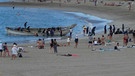 Flüchtlinge landen im Dezember 2020 in einem offenen Boot am Strand von Los Cristianos auf Teneriffa zwischen sich sonnenden Touristen. | Bild: picture alliance/dpa | Andreas Jütte
