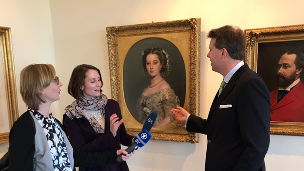 Hubertus Prinz von Sachsen-Coburg und Gotha, steht im ersten Stock seines Familienschlosses. Hier wird er interviewt von den BR Reporterinnen Alexandra Rinschler (links mit Mikro) und Regina Kirschner. | Bild: BR