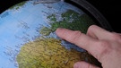 Ein Finger auf einem Globus | Bild: picture-alliance/dpa