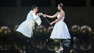 Zwei Frauen in weißen Kleidern auf einer Theaterbühne, die ein reicht der anderen eine Rose | Bild: Anna-Maria Löffelberger/Salzburger Landestheater