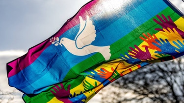 Weiße Friedenstaube auf einer bunten Fahne  | Bild: picture-alliance/dpa