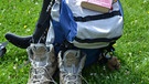 Rucksack, Bibel und Wanderschuhe liegen auf einer Wiese. | Bild: Elisabeth Friedgen/ifp
