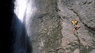Eine Frau klettert neben einem Wasserfall die Felsenwand hinauf. | Bild: picture-alliance/dpa