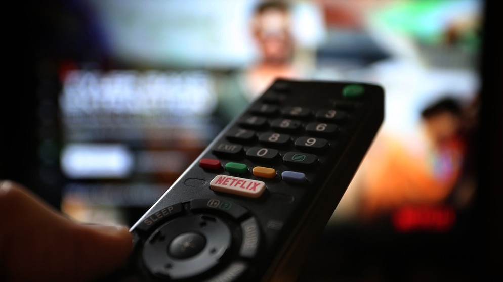 Fernbedienung mit Netflix Taste die vor einem Fernseher gehalten wird | Bild: picture alliance / dpa-tmn | Karl-Josef Hildenbrand