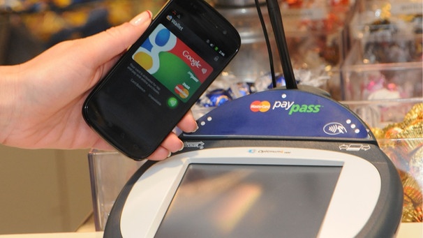 Ein Handy wird an einer Supermarkt-Kasse neben ein Gerät zur elektronischen Zahlungsabwicklung gehalten. | Bild: picture-alliance/dpa