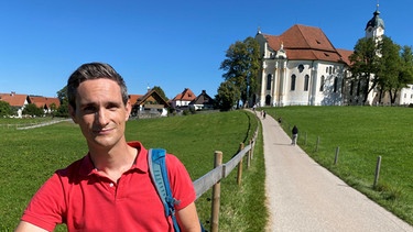 STATIONEN-Modertaor Benedikt Schregle vor der Wallfahrtskirche zum Gegeißelten Heiland auf der Wies in Steingaden | Bild: BR/ Elisabeth Möst 