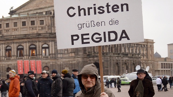 Teilnehmer einer Veranstaltung der Pegida demonstrieren am 25.01.2015 in Dresden und halten ein Schild hoch "Dresdner Christen grüßen die Pegida"  | Bild: picture-alliance/dpa