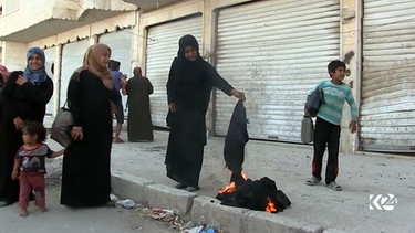 Ein Screenshot aus einem Video, das vom Sender Kurdistan 24 veröffentlicht wurde, zeigt Frauen, die am Straßenrand Nikabs, schwarze Gesichtsschleier, verbrennen. | Bild: picture-alliance/dpa/Kurdistan24