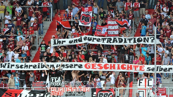 Die Fans des 2004 gegründeten FC Ingolstadt halten Transparente in die Höhe, auf denen steht "Ihr und Eur Tradition? Wir schreiben unsere Geschichte selber!". (14.08.2011) | Bild: picture-alliance/dpa