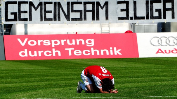 Ingolstadts Markus Karl liegt vor einem Transparent mit der Aufschrift "Gemeinsam 3. Liga" auf dem Rasen. | Bild: picture-alliance/dpa