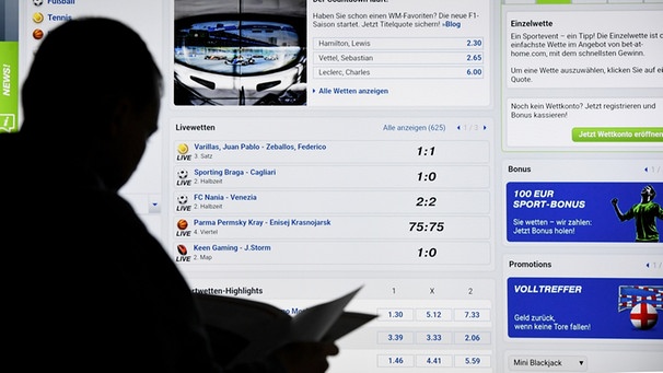 Ein Mann steht vor einem Bildschirm mit einer Seite eines Anbieters für Sport-Wetten. | Bild: Carsten Rehder/dpa
