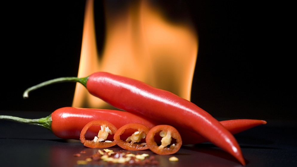 Scharfe Chilis mit Feuer im Hintergrund. Die Schärfe löst einen "Pepper-high" im Mund aus und kann süchtig machen. | Bild: picture-alliance/dpa