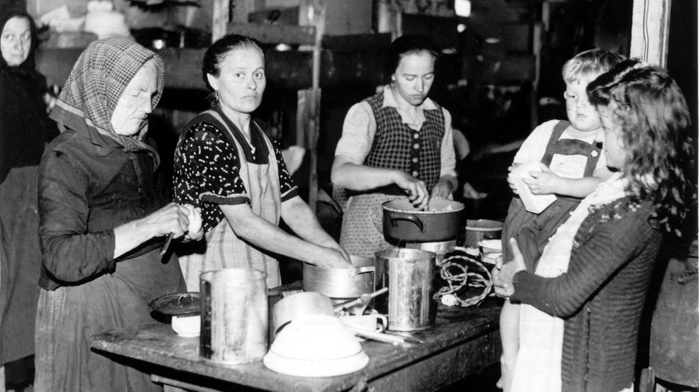 Frauen bereiten 1948 an einem Tisch im Flüchtlingslager Allach Mahlzeiten zu. In dem Lager leben oft 30 bis 40 Heimatvertriebene - alt und jung, Männer und Frauen - dicht gedrängt in Gemeinschaftsräumen. Die menschenunwürdigen Unterkünfte wurden in der Öffentlichkeit heftig kritisiert.  | Bild: picture-alliance/dpa